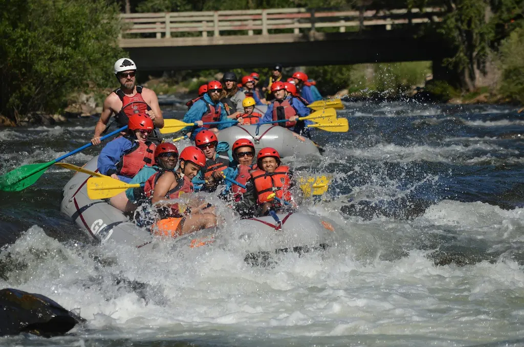 A guided raft group paddling hard through churning whitewater beneath a footbridge on a river near Durango, Colorado.