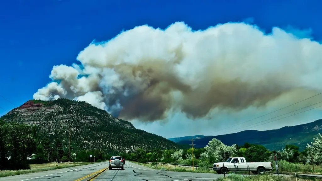 Wildfire smoke plume rising over a hillside north of Durango, seen from US Highway 550